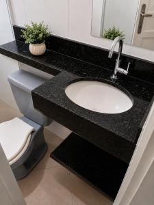 a bathroom with a black counter with a sink and a toilet at Casa centro de Peruíbe in Peruíbe