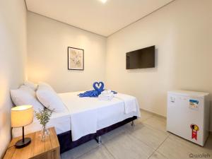 a bedroom with a bed with white sheets and a tv at Wafeh Guest House - Fleming - Bar & Jardim in Belo Horizonte
