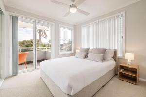 a white bedroom with a large bed and a balcony at Sandcastles 1, 8 Ala Moana Way - air conditioned townhouse with Wi-Fi and Complex Pool in Fingal Bay +28 photos