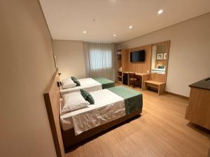 a hotel room with two beds and a desk at POUSADA MILÊNIO LTDA in Ponte Nova