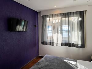 a bedroom with a purple wall with a tv on the wall at Center Verdes Pássaros Loft in Porto Alegre +10 photos