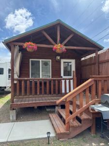 a house with a large deck with two flower baskets at Tiny Yellowstone Riverside Cabin in Gardiner +3 photos