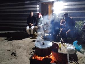 a group of people sitting around a pot on a fire at Mujib Castle Gate Camp in Dhībān