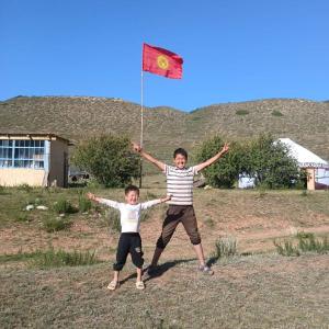 two young boys standing in a field flying a kite at Актан in Chong-Kyzylsu