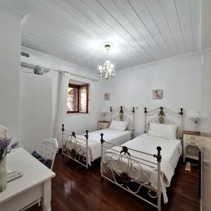 two beds in a white bedroom with a chandelier at Casa di Sofiana by wood and stone in Áyios Pétros