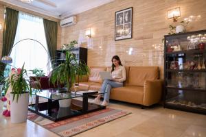 Eine Frau sitzt mit einem Laptop auf einem Sofa im Wohnzimmer. in der Unterkunft Garden Hotel in Bischkek