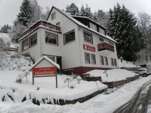 ein schneebedecktes Haus mit einem Schild davor in der Unterkunft Pension Hamburg in Bad Grund