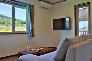 a living room with a couch and a tv and windows at Retreat Furano A in Furano