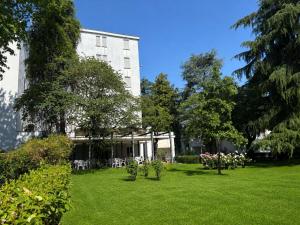 a white building with a green yard with trees at Hotel Terme in Monticelli Terme