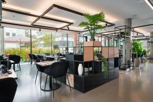 ein Restaurant mit schwarzen Stühlen, Tischen und Pflanzen in der Unterkunft GREFIS Hotel München-Gräfelfing in München