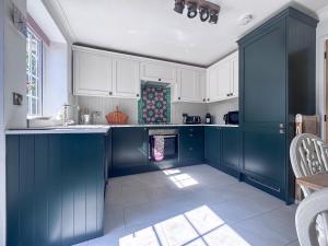 a blue kitchen with white cabinets and a sink at Little Tern in Snettisham