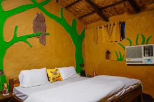 a bedroom with a bed with a tree painted on the wall at Camp Hornbill Corbett in Rāmnagar