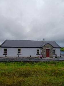 a white house with a red door in a field at Liam's Cottage Bed and Breakfast in Lisdoonvarna