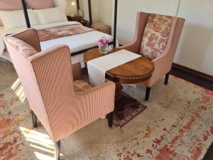 a bedroom with a bed and two chairs and a table at Amourette's Rose Cottage in Centurion