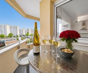 a bottle of wine and two glasses on a table with roses at Porte de Paris, spacieux T3, terrasse et parking in Vanves