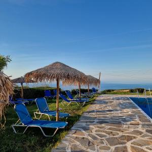 a row of chairs under a straw umbrella and the ocean at Bellevue Village ''Αdults Only'' in Agia Pelagia