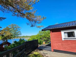 a red house with a fence next to a lake at Stuga 21 i Dalskärs Camping in Bergkvara