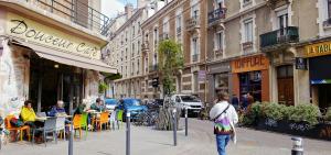 a woman walking down a city street with tables and chairs at Avocado - Garage inclus - T3 - 96m2 - lumineux - Centre ville tout à pied in Grenoble