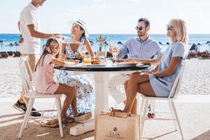 a group of people sitting around a table on the beach at Elia Mykonos Resort in Elia Beach