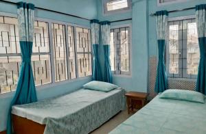 two beds in a bedroom with blue walls and windows at D Mukta Lodge in Guwahati