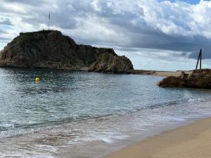 a beach with a rock island in the water at Lupe Mediterranean Loft,150m from the Beach Blanes Center in Blanes +3 photos