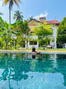 a man laying in a swimming pool in front of a house at Sunny's Garden Hotel in Ambalangoda