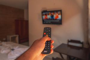 a hand holding a remote control in front of a tv at Pousada Acqua Bella PISCINA CLIMATIZADA in Bertioga