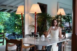 a woman sitting at a table with a cup of coffee at Adigars Manor Kandy - A Boutique Heritage Hotel Built in 1804 in Kandy