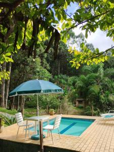 a table and chairs with an umbrella next to a swimming pool at Chácara Luz do Vale in Votuverava