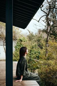 a woman sitting on a porch looking out at trees at Satologue in Okutama