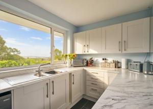 a kitchen with white cabinets and a large window at Sea Gem - large holiday cottage in Tenby with private parking in Tenby