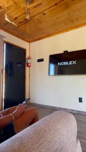 a person sitting on a couch with a tv on a wall at Cabañas Los Robles Premium in Villa Quillinzo