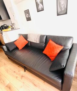 a black leather couch with orange pillows in a living room at Le studio terrasse Béthunois - Appart hôtel centre climatisé - All confort in Béthune