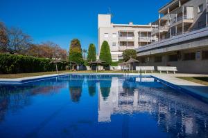 a swimming pool with benches and umbrellas in front of a building at AT098 Pau Casals in Torredembarra