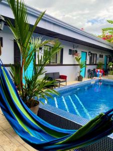 a hammock by a swimming pool in front of a house at Hotel Perico Azul & Surf Camp in Jacó