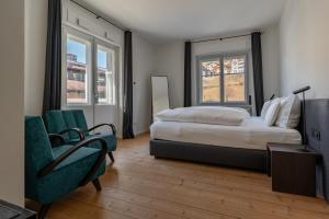 a bedroom with a bed and a chair and two windows at Casa al Sole in Ortisei