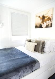 a white bedroom with a bed with a cow picture on the wall at NEW! Cozy Container Home at Cliffside #2 in Orderville