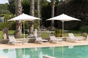two white umbrellas and chairs next to a pool at Masseria Tenuta Specolizzi in Lido Marini
