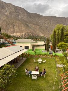 two people sitting at tables in a yard with mountains at Madina Hotel 2 in Gilgit
