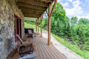 a wooden porch with chairs and a stone wall at High Road Cabin in Banner Elk +13 photos