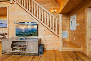 a living room with a tv and stairs in a log cabin at Alpine Ridge in Banner Elk