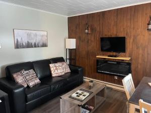 a living room with a black leather couch and a flat screen tv at Lush's Cottages in Cormack