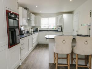 a kitchen with white cabinets and a counter with two stools at 9 Beckett Close in Colwyn Bay