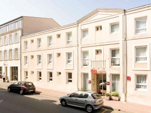 two cars parked in front of a large white building at ibis Rochefort in Rochefort