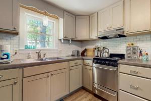 a kitchen with white cabinets and a sink and a stove at The Woodland Cottage in Eastham +10 photos