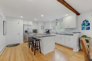 a white kitchen with white cabinets and bar stools at The Blue Whale Cottage in Brewster