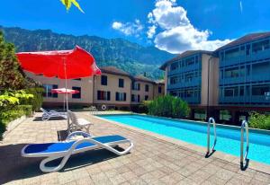 a swimming pool with a red umbrella and chairs next to a building at Seeparadiesli am schönen Thunersee in Därligen