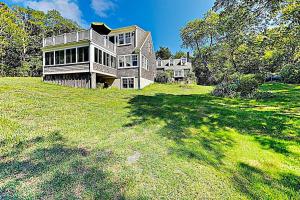 a large house on a grassy field with trees at Brookview Bungalow in South Wellfleet