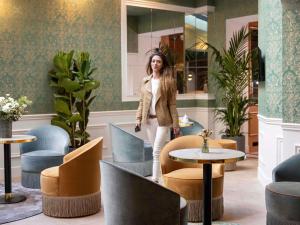 a woman standing in a lobby with chairs and tables at Hotel Mercure La Sorbonne Saint-Germain-des-Prés in Paris