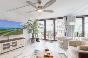 a living room with a ceiling fan and large windows at Waves & Palms Oasis in Marco Island